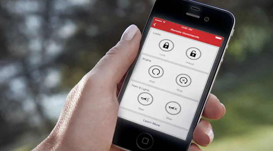 Hand holding a cell phone with the My Chevrolet Rewards app / My GM Rewards app displayed, including buttons for remote start and vehicle locks