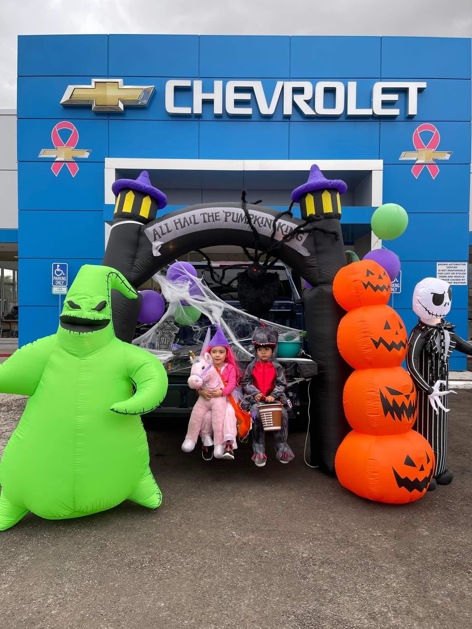 Two kids in Halloween costumes pose in front of a spooky trunk display at a Chevrolet dealership